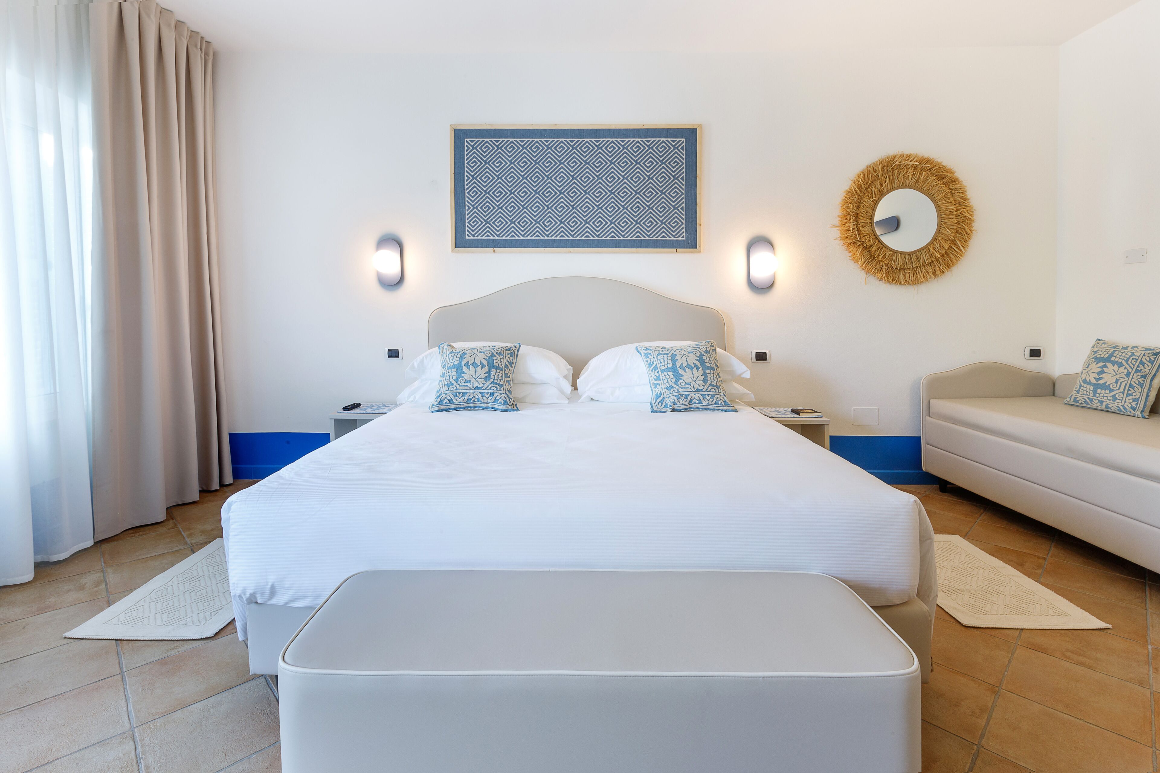 A bedroom with a large bed, bedside tables, a sofa, and a wall-mounted mirror.
