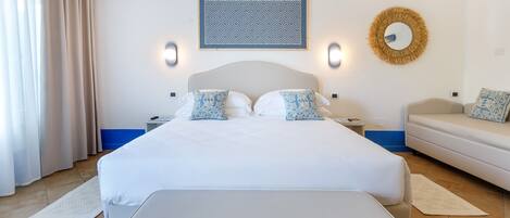A bedroom with a large bed, bedside tables, a sofa, and a wall-mounted mirror.