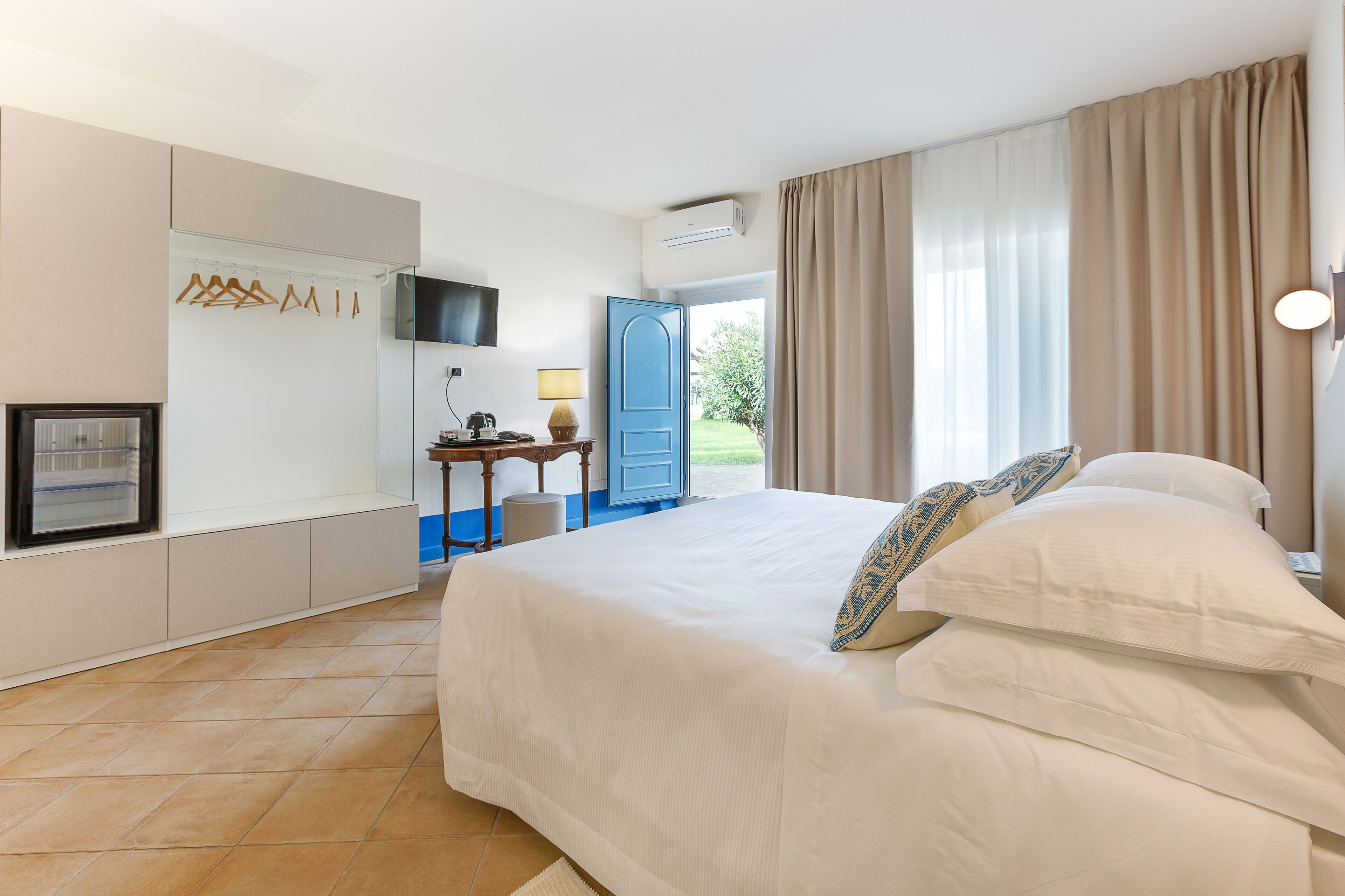 A hotel room with a large bed, a desk with a lamp, a television, and a view of the outdoors.