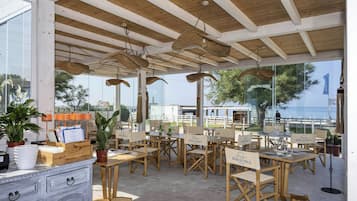 An outdoor dining area with wooden tables and chairs, a buffet counter, and a view of the sea.