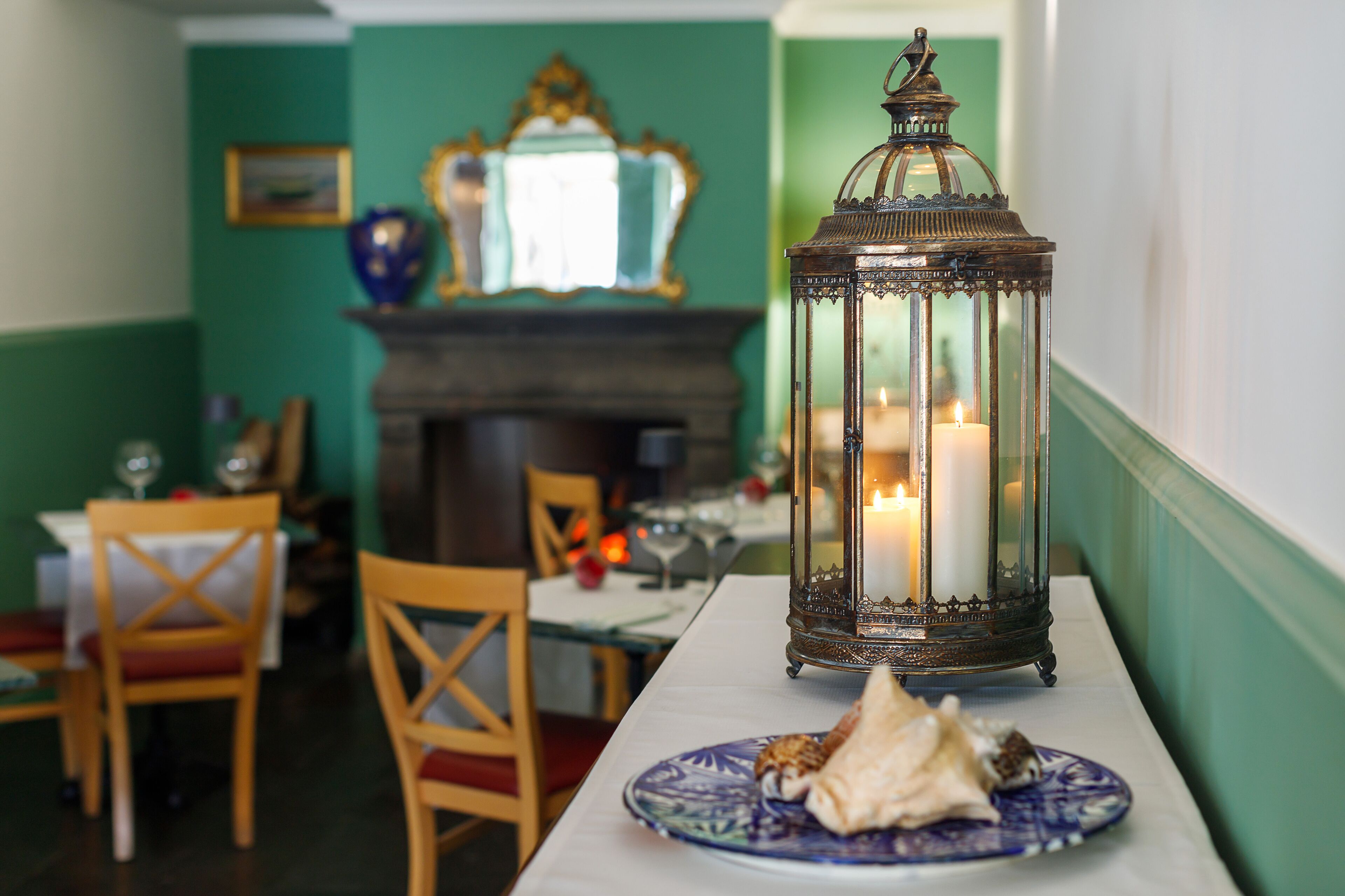 A dining area with a table set for two, a candle in a lantern, and a plate with food.