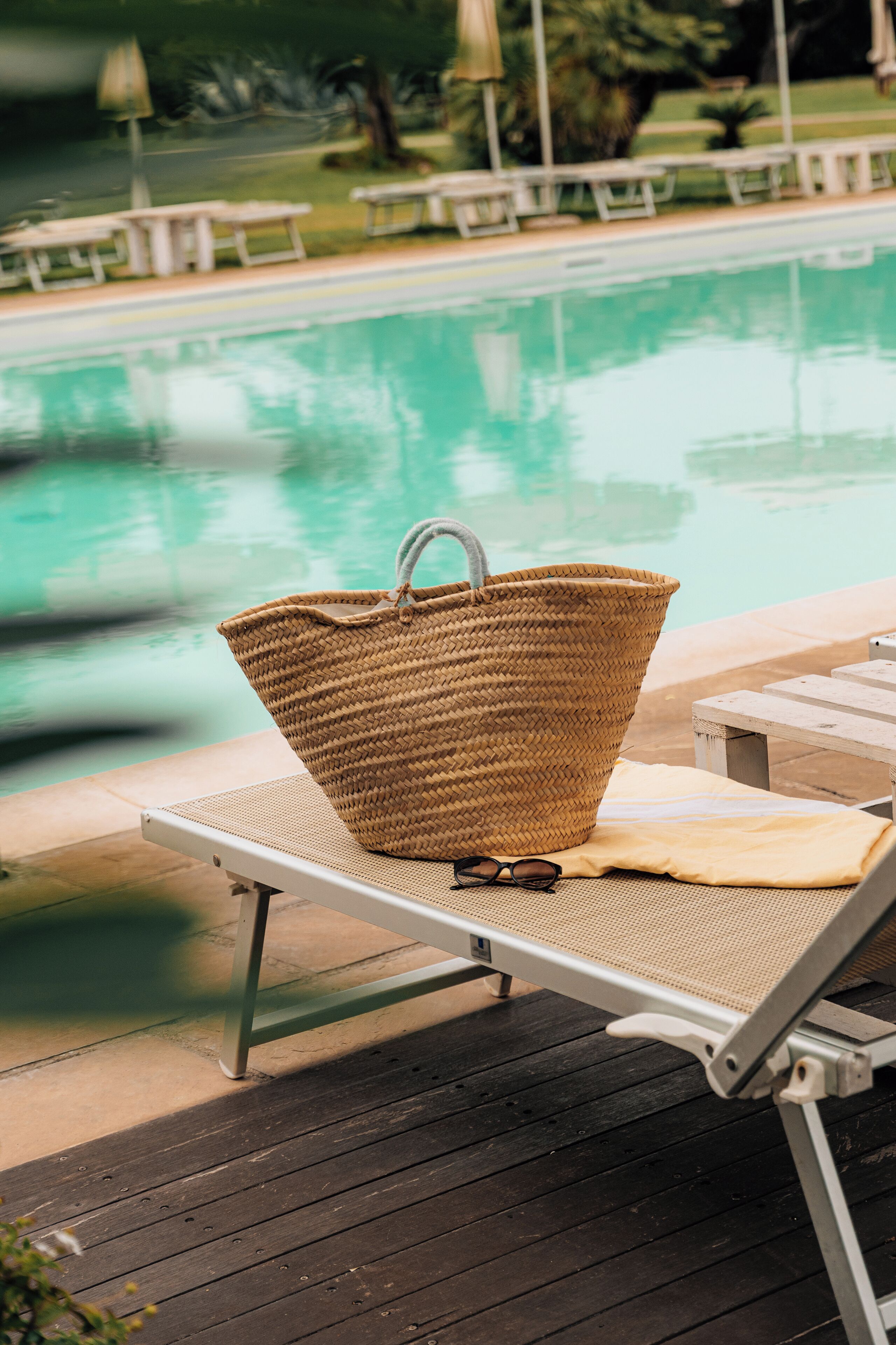 Zona junto a la piscina con una tumbona, un bolso de fibra y un par de gafas de sol sobre una alfombra.