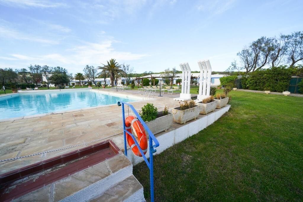 Una piscina con un flotador salvavidas, una zona verde y una estructura blanca con columnas.