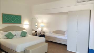Une chambre d’hôtel comprenant un lit, une table de chevet avec une lampe, une petite table avec une lampe, une armoire et un climatiseur fixé au mur.