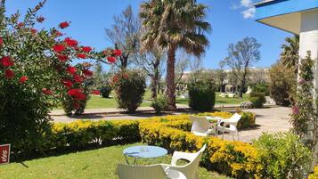 Un giardino con sedie e tavolo bianchi, circondato da siepi curate e piante fiorite.
