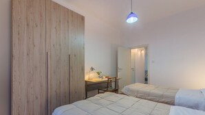 A bedroom with two beds, a wooden wardrobe, a desk with a chair, and a hanging light fixture. - GuestHost - San Donato Fiera Apartment (Bologna)