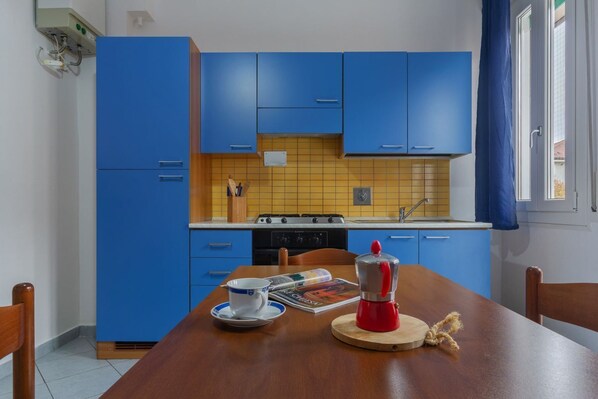 Een koelkast, een oven, een kookplaat, kookgerei, borden en bestek