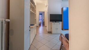 A narrow hallway with a bed, a TV, and a blue cabinet. - GuestHost - San Donato Fiera Apartment (Bologna)