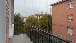 A balcony with a metal railing, a tiled floor, and a view of neighboring buildings and trees. - GuestHost - San Donato Fiera Apartment (Bologna)
