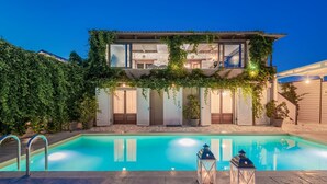 Una casa de dos pisos con piscina, paredes de piedra y un patio cubierto.