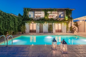 Une maison à deux étages dotée d’une piscine, de murs en pierre et d’un patio couvert.