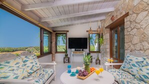 Una zona de estar exterior acogedora con pared de piedra, televisor de pantalla plana y una mesa con fruta y bebidas.