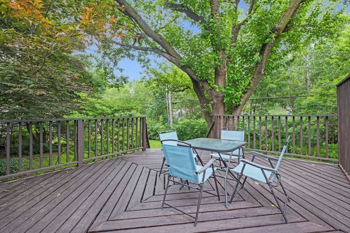 A wooden deck with a table and chairs, surrounded by trees and a fence.