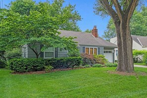 A residential house with a well-maintained lawn, a large tree, and a brick pathway leading to the entrance.