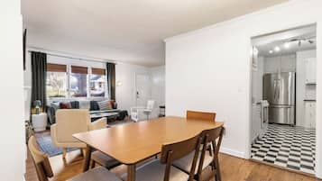 Eine moderne Küche mit Edelstahlgeräten, ein Essbereich mit Holztisch und -stühlen sowie ein Wohnzimmer mit Sofa und Sesseln.