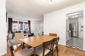 A modern kitchen with stainless steel appliances, a dining area with a wooden table and chairs, and a living room with a sofa and chairs.