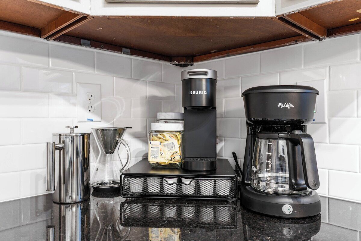 Uma cozinha com cafeteira, chaleira, moedor de café e jarra de café no balcão.