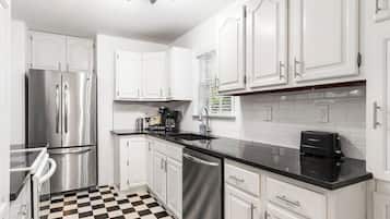 A modern kitchen with white cabinets, stainless steel appliances, and a black and white checkered floor.