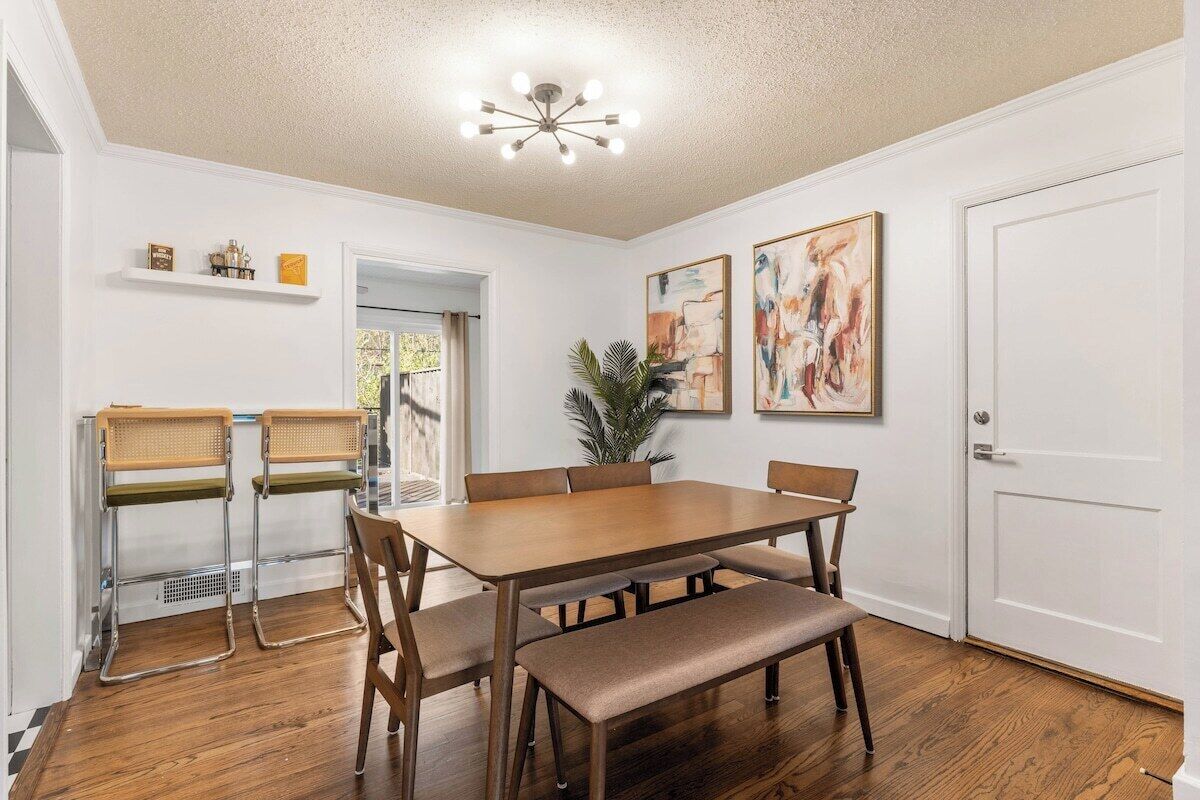 A dining area with a wooden table, chairs, and a bench. There are two wall-mounted shelves with decorative items.