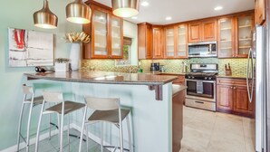 Una cocina con una isla central, taburetes de bar, armarios de madera, electrodomésticos de acero inoxidable e iluminación colgante.