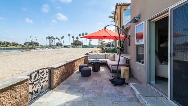 Un patio con mobiliario exterior, una sombrilla roja y vista a la playa.