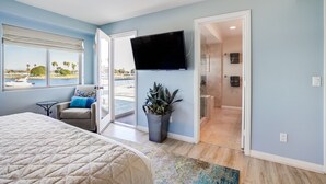Un dormitorio con cama, una silla, televisor, planta y vista al mar.