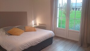 Un dormitorio con cama, lámpara de noche y ventana con vistas a un jardín y un edificio.