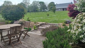 Una terraza de madera con una mesa y sillas, rodeada de plantas diversas y un césped.