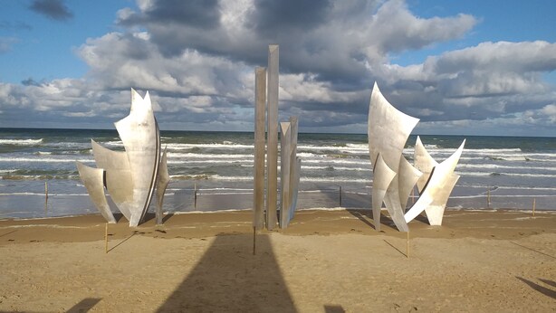 Una playa con esculturas abstractas y el océano al fondo.