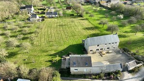 Vista aérea de una propiedad rural con un gran edificio de piedra, césped bien cuidado y árboles dispersos.