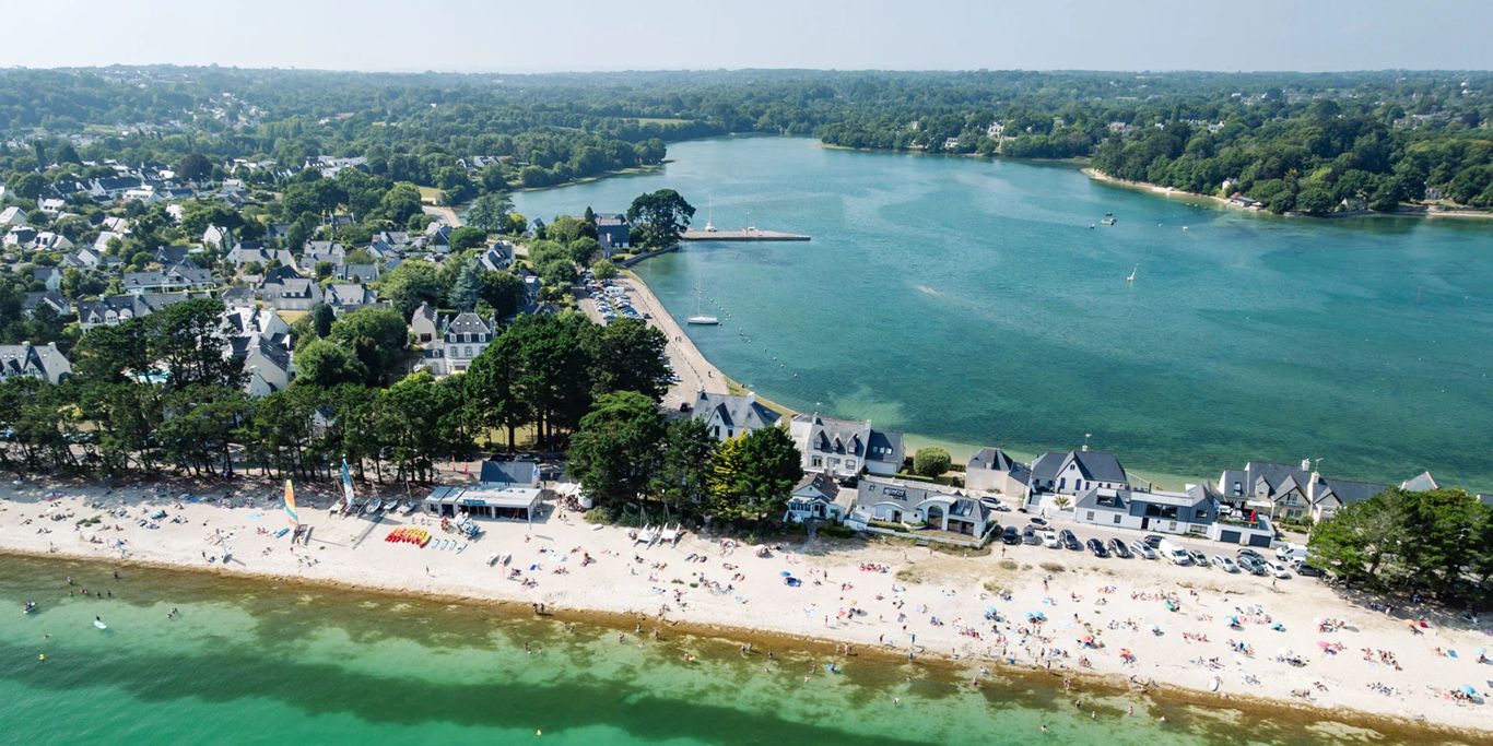 An aerial view of a coastal town with a beach, houses, and a river.