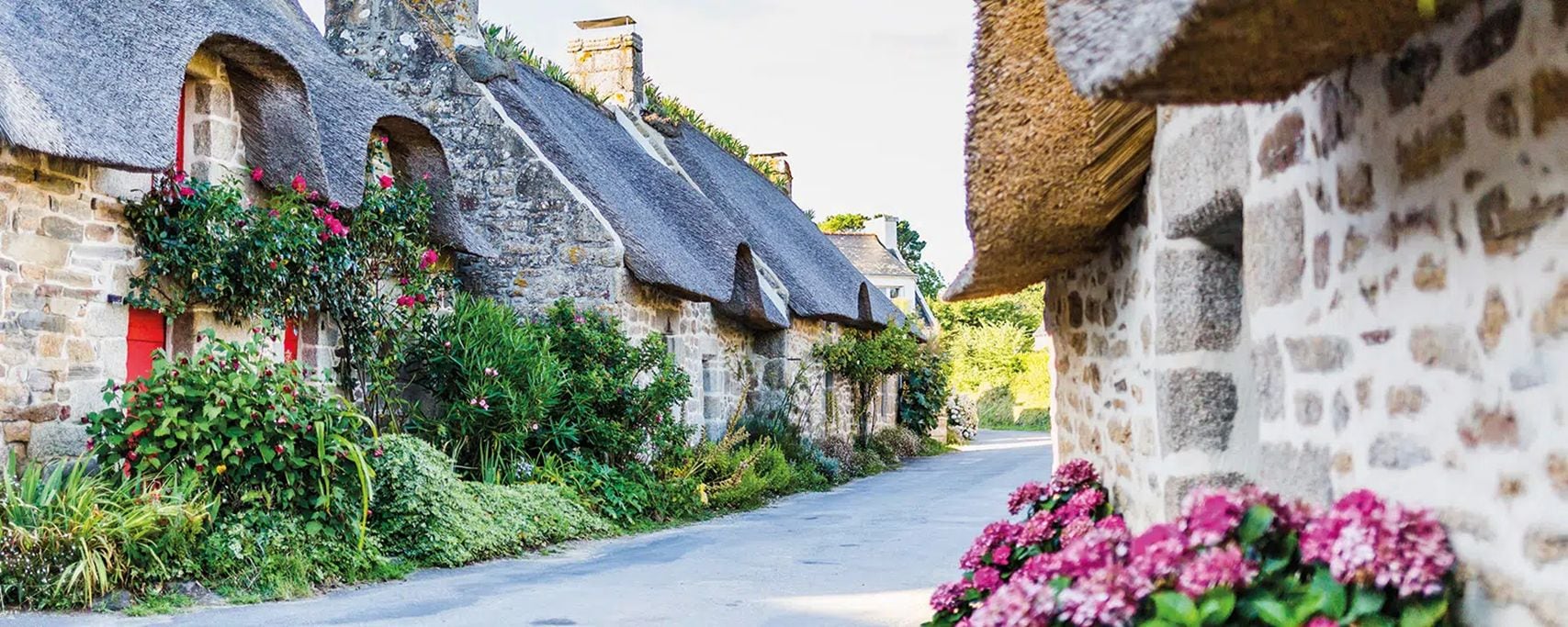 A narrow street lined with stone buildings with thatched roofs and red window shutters.