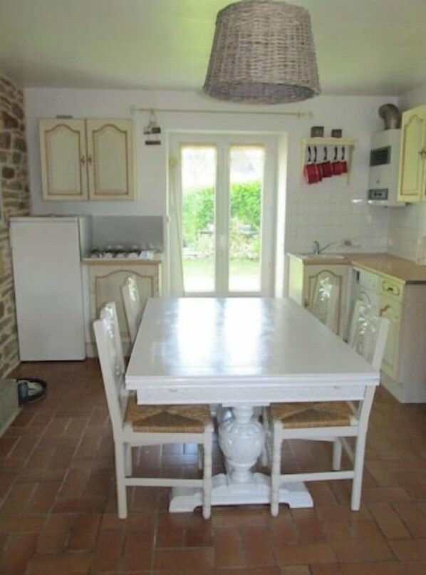 A kitchen with a white table, chairs, and cabinets. There is a window with a view of greenery outside.