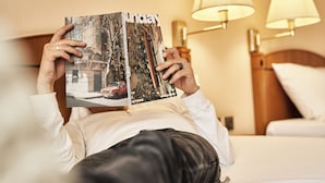 Una persona recostada en una cama leyendo una revista.