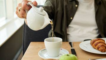 Una persona sirve té en una taza sobre una mesa con un croissant, una manzana y una naranja.