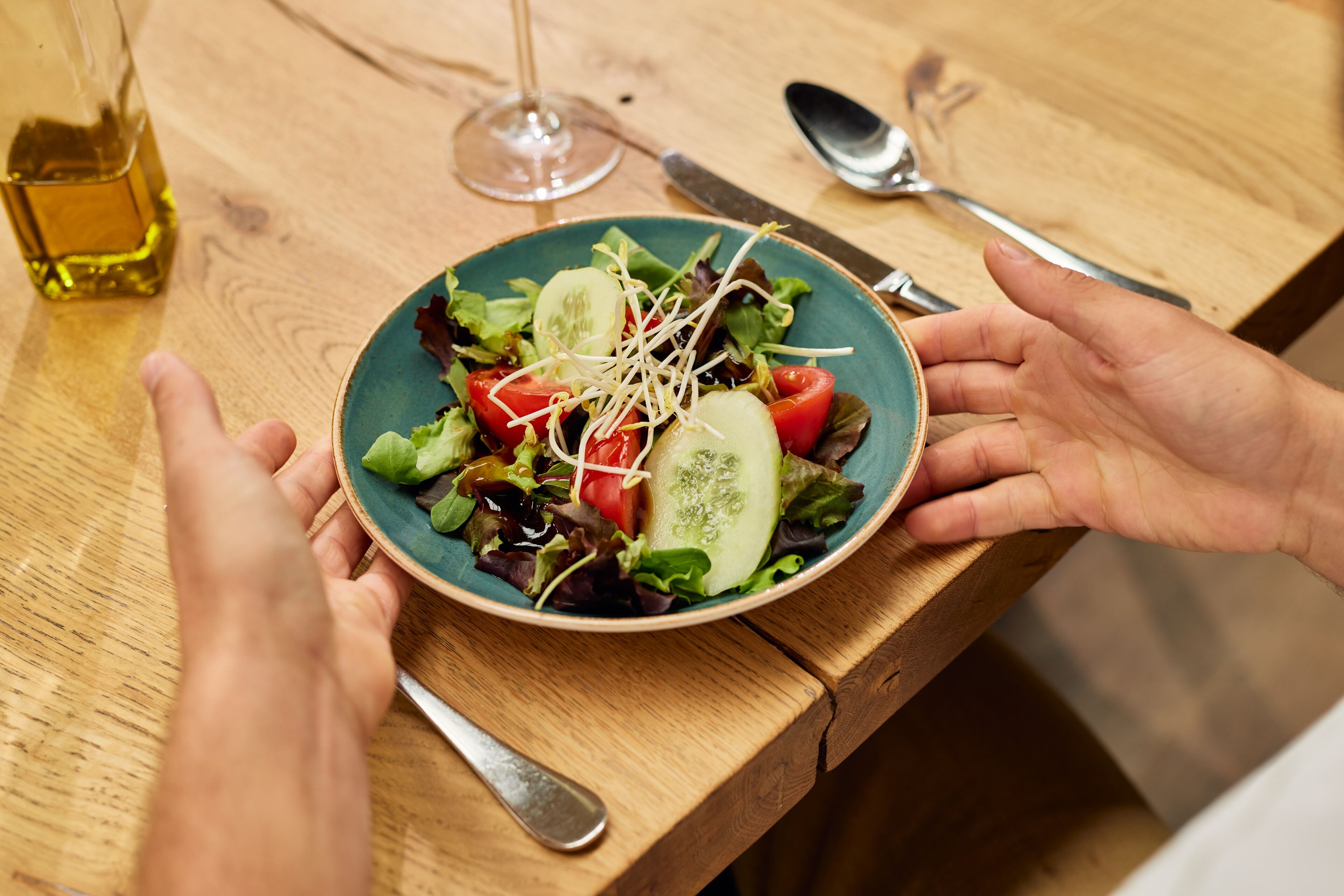 A wooden table with a plate of salad, a glass of wine, and cutlery.