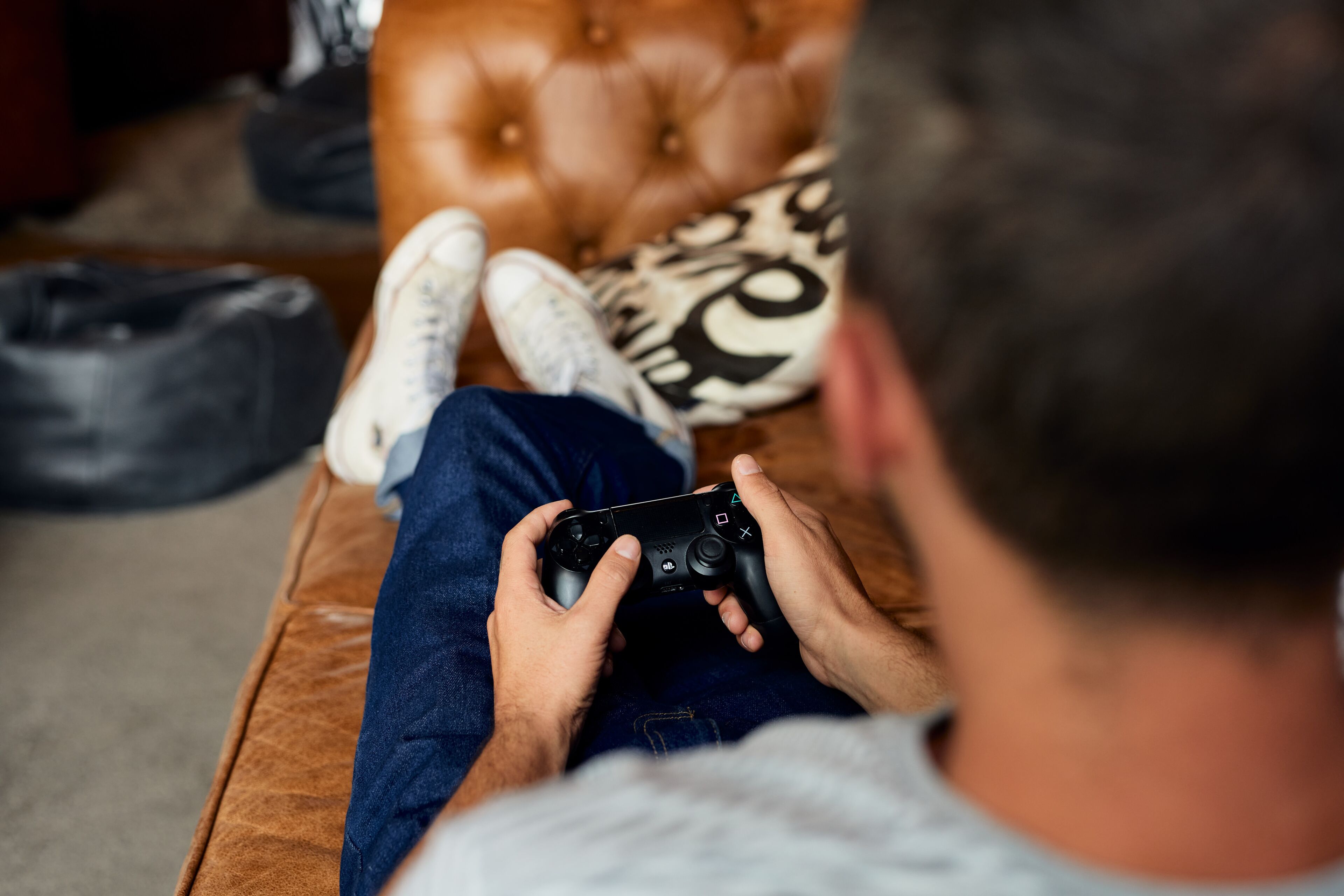 Uma pessoa sentada em um sofá marrom com tufos, segurando um controle de videogame preto.