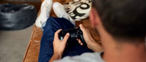 Uma pessoa sentada em um sofá marrom com tufos, segurando um controle de videogame preto.
