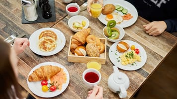 A breakfast setting with various dishes, including croissants, eggs, and fruits, on a wooden table.