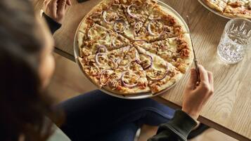 Eine Person sitzt an einem Holztisch mit einer Pizza und einem Glas Wasser.