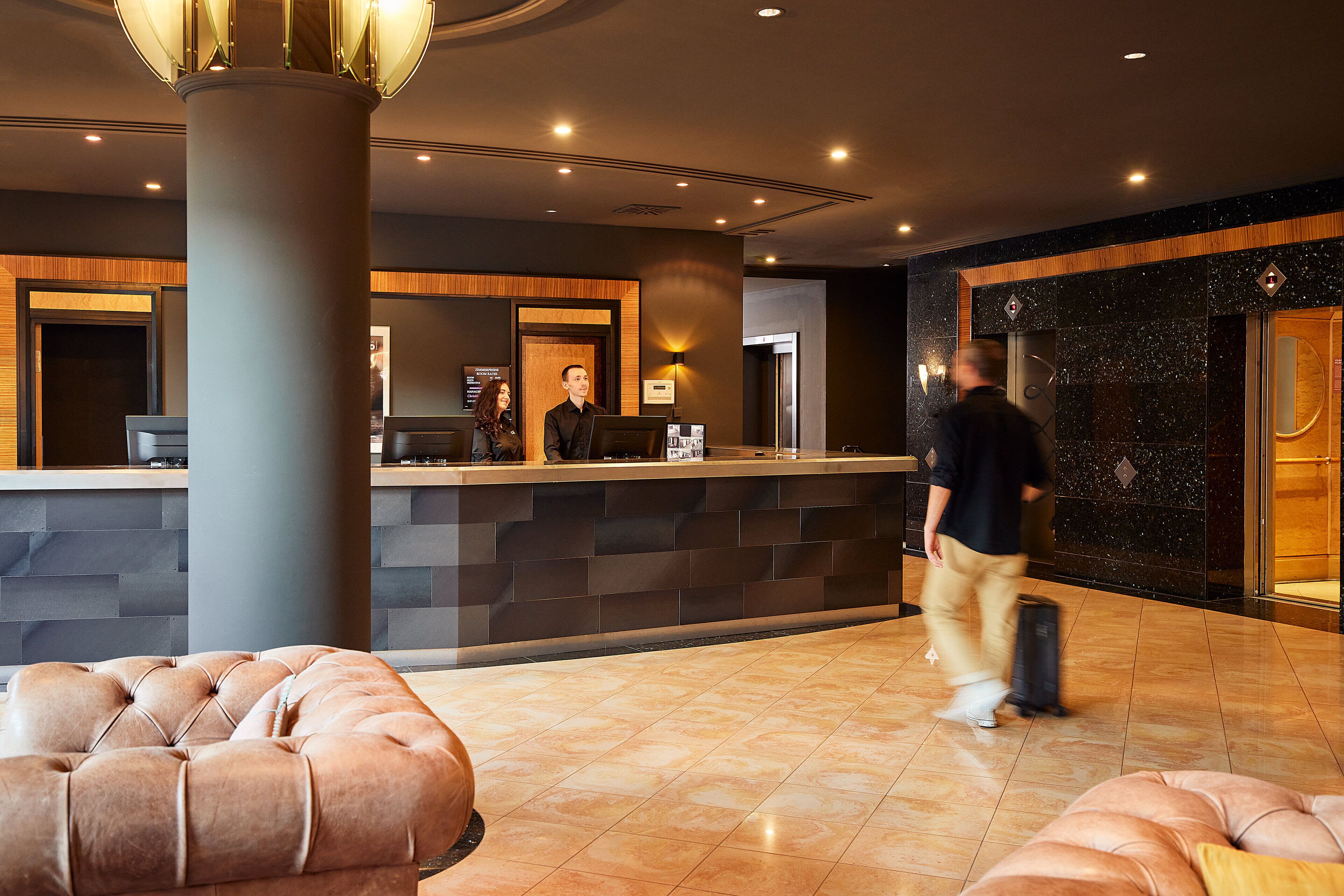 A hotel lobby with a reception desk, a large pillar, and plush seating areas.
