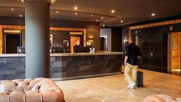 A hotel lobby with a reception desk, a large pillar, and plush seating areas.
