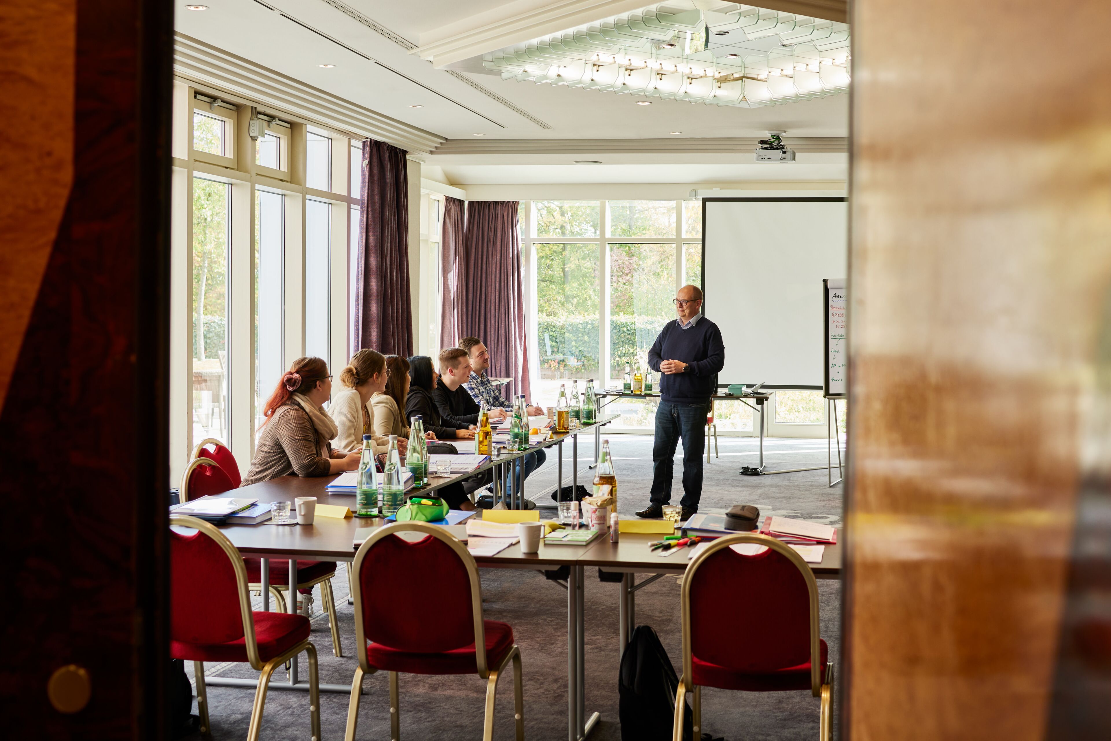 Ein Konferenzraum mit einem großen Tisch, roten Stühlen und einem Referenten am Vorsitzen.