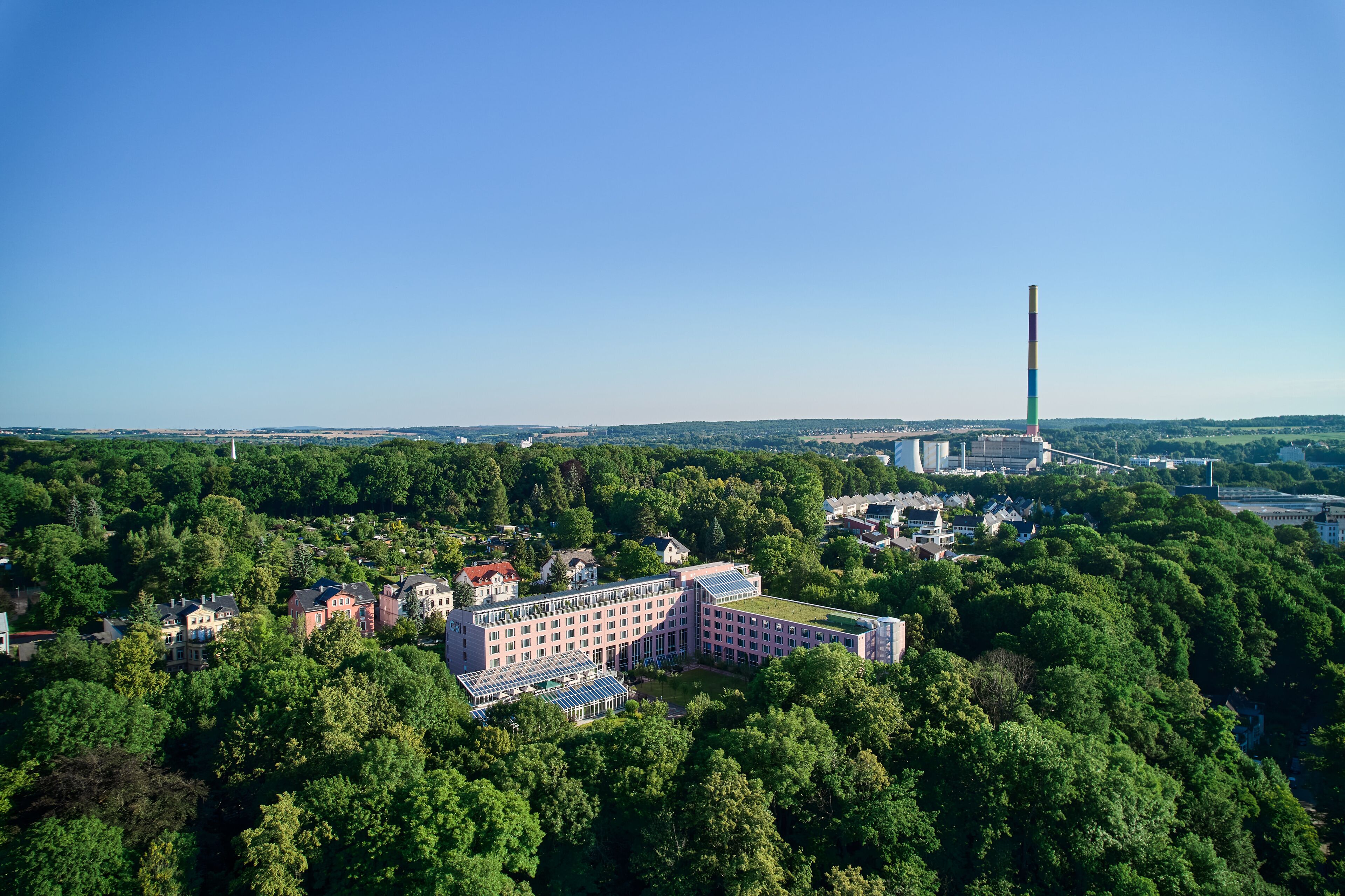 An aerial view of a large building surrounded by dense greenery, with a prominent tower in the background.