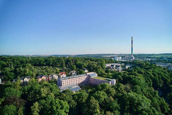An aerial view of a large building surrounded by dense greenery, with a prominent tower in the background.