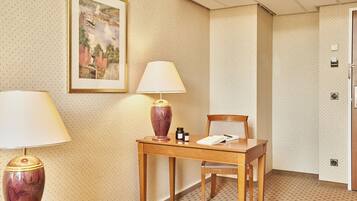 Habitación de hotel con un escritorio de madera, dos lámparas, una silla, un cuadro en la pared y una puerta con manija.