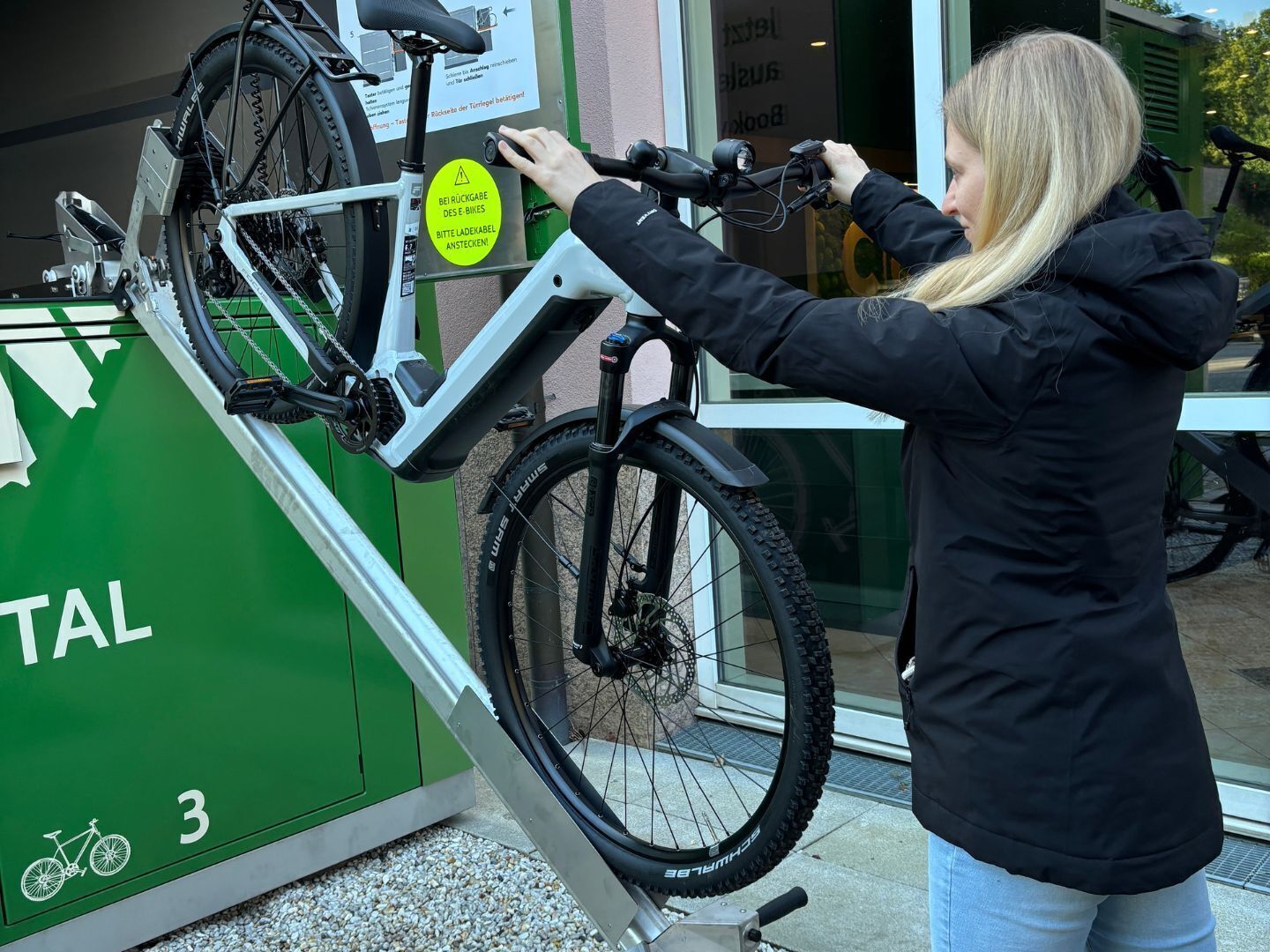 Une personne qui déverrouille un vélo à une station reconnaissable à un panneau vert portant le numéro 3.