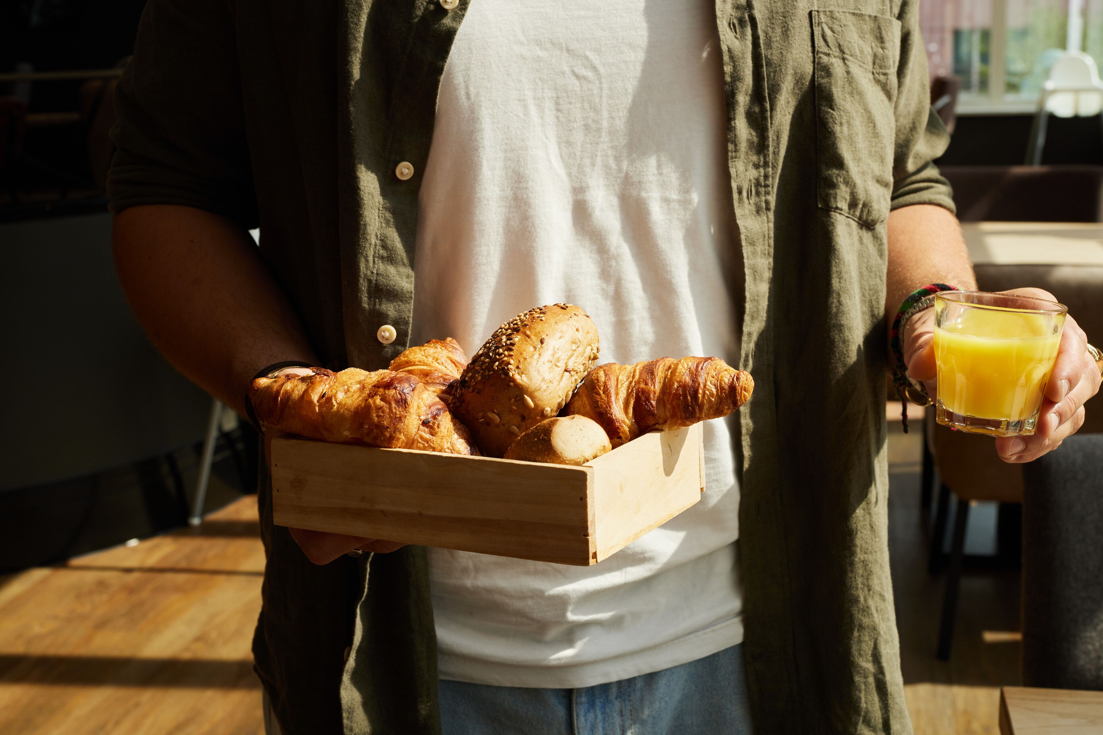 Una persona sosteniendo una caja de madera con croissants y un vaso de jugo de naranja.