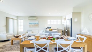 Un soggiorno moderno e luminoso con zona pranzo, cucina e un'ampia finestra vista spiaggia.