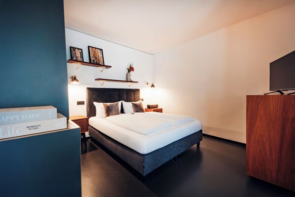 Una habitación de hotel moderna con una cama grande, mesitas de noche, un armario y un estante de pared con adornos.
